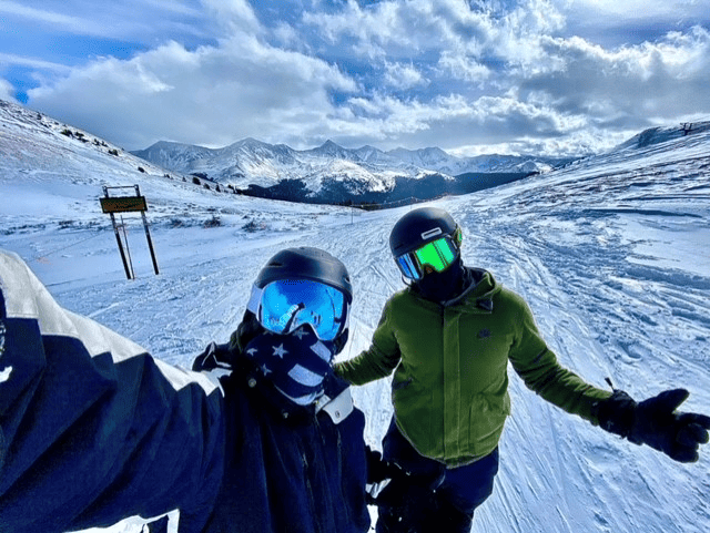 Two skiers on the slopes of Breckenridge Ski resort talking a selfie with snow and mountains in the background